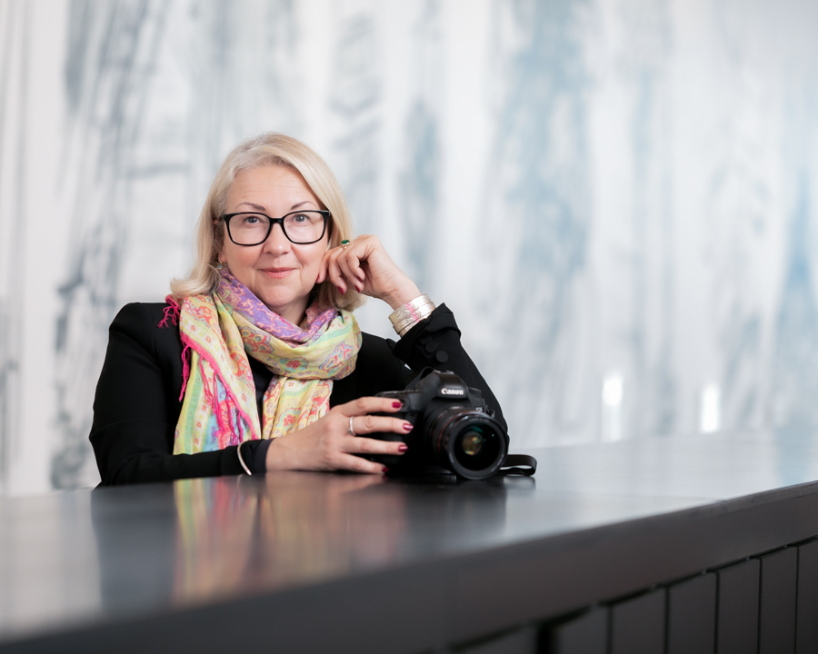 Cherry wearing a brightly coloured scarf holding her Canon camera smiling at the screen for her headshot